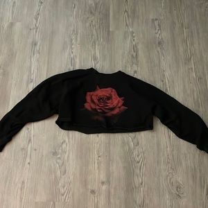 This is a cropped  long sleeved black sweater with a red rose on the center